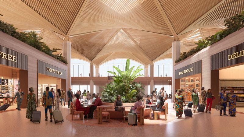 Passengers walking through the bright duty-free retail area with indoor tropical plants and vaulted wooden ceilings.