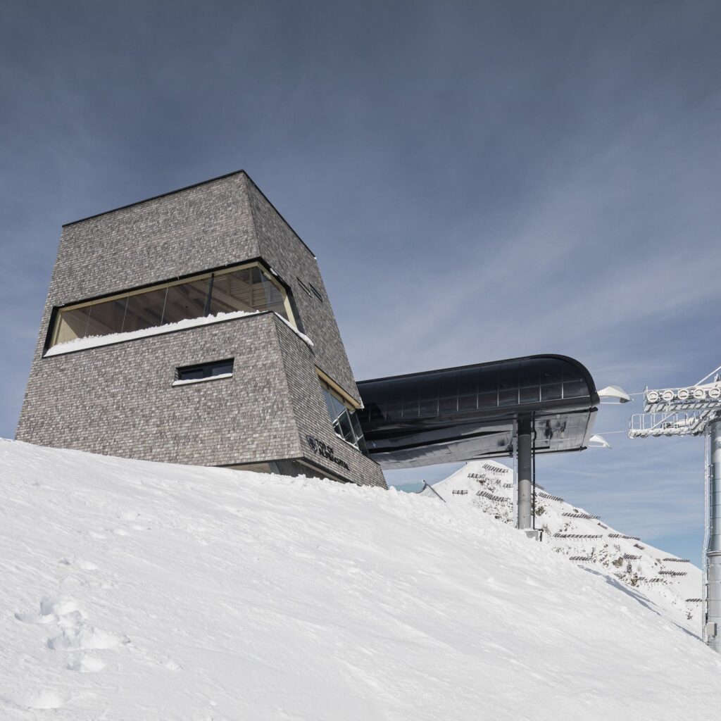 برج جبال الألب الخشبي يقف متصلاً مباشرة بمحطة مصعد تزلج زجاجية سوداء على منحدر ثلجي