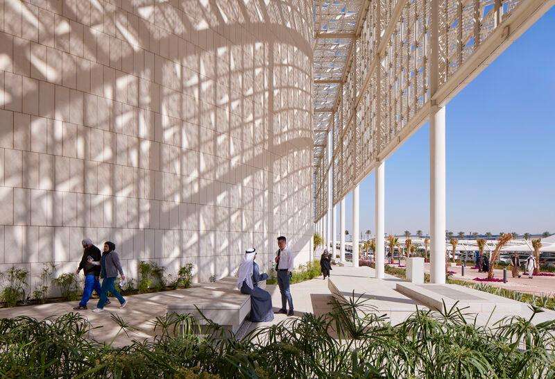 طلاب يتجمعون تحت الظل الواقي لمظلة معمارية شبكية كبيرة.