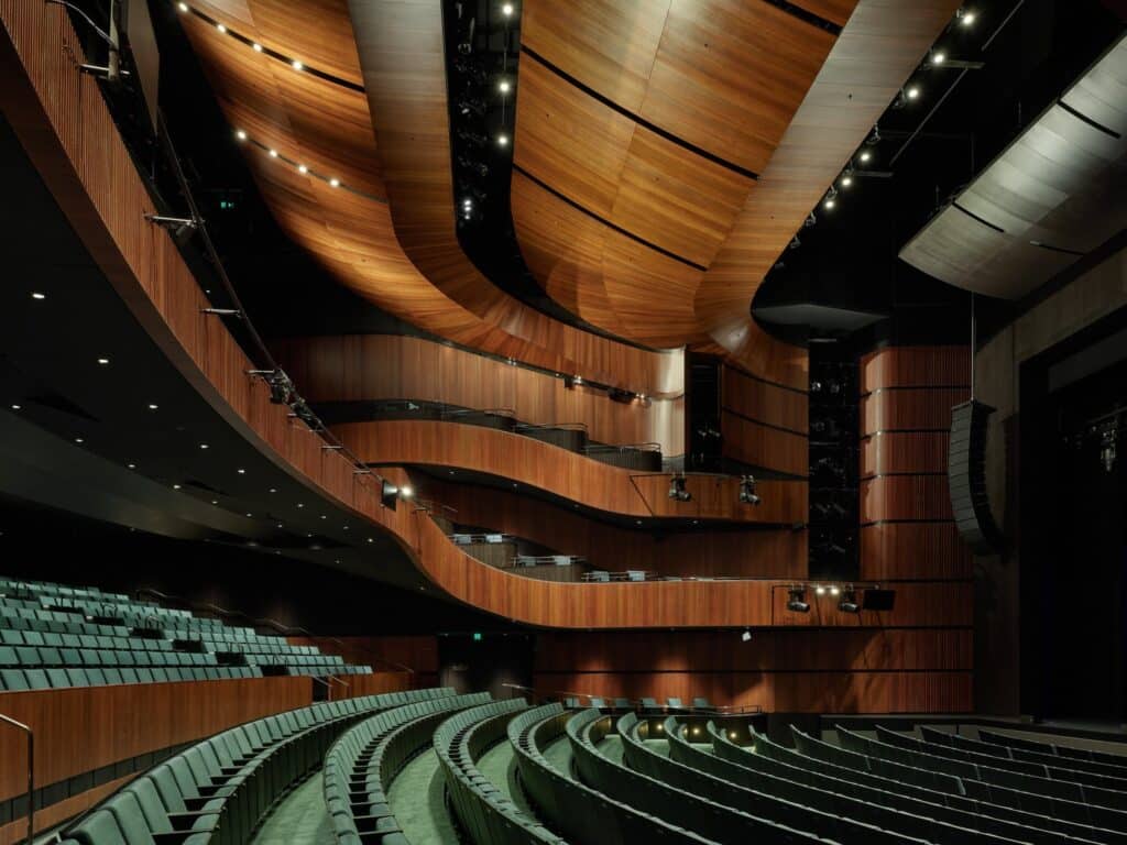 Curved wooden acoustic panels and green seating inside a modern performance auditorium