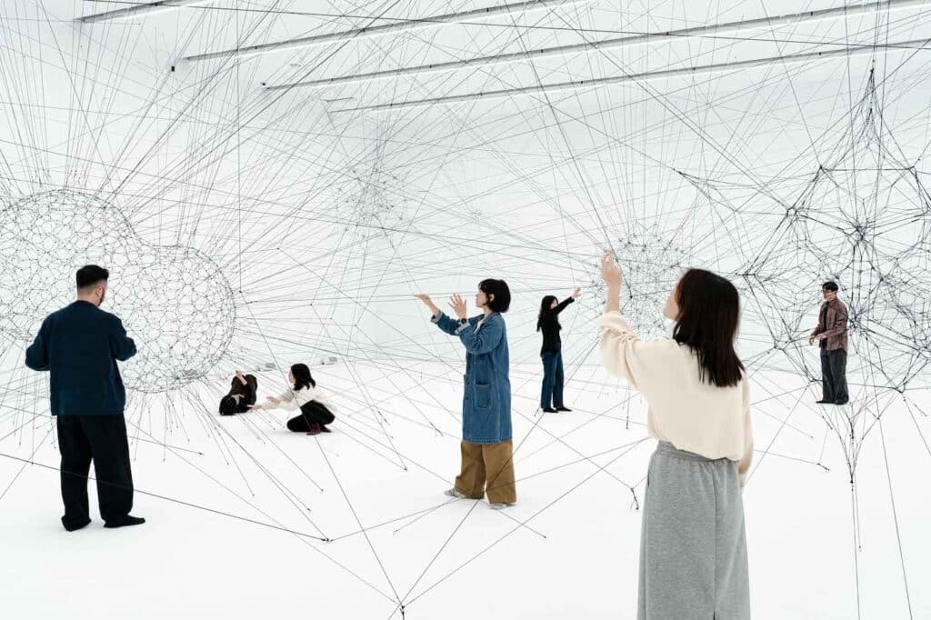 Wide view of people exploring an interactive architecture space filled with geometric tensile webs