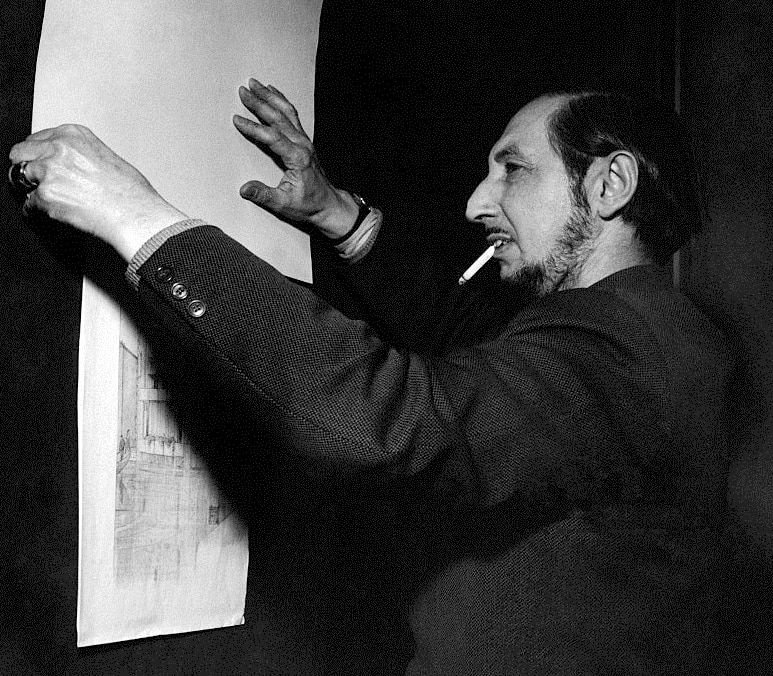 المعماري كارلو سكاربا يدخن سيجارة أثناء فحص رسومات معمارية على الحائط.