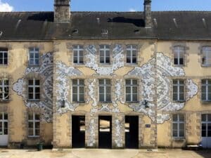 When Lace Becomes Architecture Some artists build a visual language so consistent and so precise that it becomes immediately legible across any surface, any city, any scale. NeSpoon, the Warsaw-based street artist, is one of them. For fifteen years, she has been translating the intricate geometry of traditional Polish lace, specifically the handmade Koniaków patterns originating from the Silesian Beskids, into monumental murals, ceramic installations, and ephemeral street works that now exist across more than 100 cities in 40 countries. Her work has appeared at the Louvre-Lens Museum, the Polish Pavilion at Expo 2020 in Dubai, and the European Parliament. She is currently developing a project connected to the reopening of the Pergamon Museum in Berlin. These are not incidental institutional appearances. They reflect a sustained critical recognition of what NeSpoon is actually doing: rescuing an anonymous, feminine, centuries-old craft tradition from the margins of cultural memory and returning it, enlarged, abstracted, and placed on the most visible surfaces of contemporary urban life. The Mural at DOMOTEKA The new commission is a large-scale mural being created in the main hall of DOMOTEKA Design Centre, Warsaw's first retail destination entirely dedicated to design, located less than twenty minutes from the city centre. Work began in March 2026, with the piece scheduled for completion by the end of the month. Visitors to the venue can observe the process live, from initial sketches through to final detail. The choice of location is worth examining. DOMOTEKA is not a gallery or a museum. It is a commercial design centre housing over 600 brands. The decision to invite NeSpoon to create a permanent mural in its primary circulation space is a statement about the relationship between retail, design, and public art, and about what kind of experience a design-focused commercial venue can credibly offer beyond the transactional. Agata Brzezińska, Senior Director and Head of CEE at Pradera, the fund that owns DOMOTEKA, framed the invitation as a natural continuation of the venue's identity: a place oriented toward quality, design, and interior architecture that aims to be more than a commercial space. Art here is not decoration. It is meant to generate a different kind of engagement with the space. The Source Material: Koniaków Lace Understanding the mural requires understanding the source. Koniaków lace is a craft tradition associated with the village of Koniaków in southern Poland, produced almost exclusively by women using needles and thread, with patterns passed between generations without written documentation. The designs are characterised by radial symmetry, dense interlocking curves, and a structural logic that is at once highly decorative and geometrically rigorous. NeSpoon's relationship to this material is neither nostalgic nor ethnographic. What she extracts from it is the structural principle, the underlying geometry of intersection, repetition, and void, and she scales it to the dimensions of a building facade or, in this case, a commercial hall. The anonymity of the original makers is part of what she is addressing. These patterns were created by women whose names were never recorded. Placing them on the surfaces of cities is one way of insisting on their presence in cultural memory. Scale, Surface, and the Logic of the Work At a monumental scale, lace undergoes a transformation that is not merely quantitative. What reads at close range as textile, intimate, tactile, domestic, becomes at building scale something closer to structural drawing. The voids that define the pattern in fabric become negative space in a mural composition. The threads become lines. The result has been described accurately as resembling delicate openwork structures floating across facades, which is the visual quality that has made NeSpoon's murals globally circulated images: they are simultaneously recognisable as pattern and as architecture. The interior environment of DOMOTEKA presents different conditions than the exterior facade. Controlled light, a defined ceiling height, a nd a surrounding context of furniture showrooms and design objects. Interior murals of this scale carry a different relationship to the viewer: the distance is fixed, the approach is frontal, and the context is commercial rather than civic. These are not deficiencies. They are simply different spatial terms that the work must negotiate. ✦ ArchUp Editorial Insight The DOMOTEKA commission raises a question increasingly relevant in contemporary design culture: what does it mean for a commercial retail venue to commission serious public art? NeSpoon's source material, anonymous, feminine, pre-industrial craft, carries enough cultural specificity that it cannot be reduced to decorative wallpaper without remainder. The Koniaków tradition is not a generic pattern. It is geographically specific, socially embedded knowledge production that happens to generate extraordinary visual material. Whether the interior commercial context sustains that specificity, or flattens the work into atmosphere, will depend partly on how the venue contextualises the commission and partly on the intrinsic qualities of the work itself, which across very different urban environments have consistently proven durable. Conclusion The DOMOTEKA mural is a genuine test of what public art can do inside the spaces of everyday commercial life. It is worth following not as a marketing exercise but as a case study in how craft memory, street art practice, and the designed interior can meet, and what each gives up or gains in that encounter.