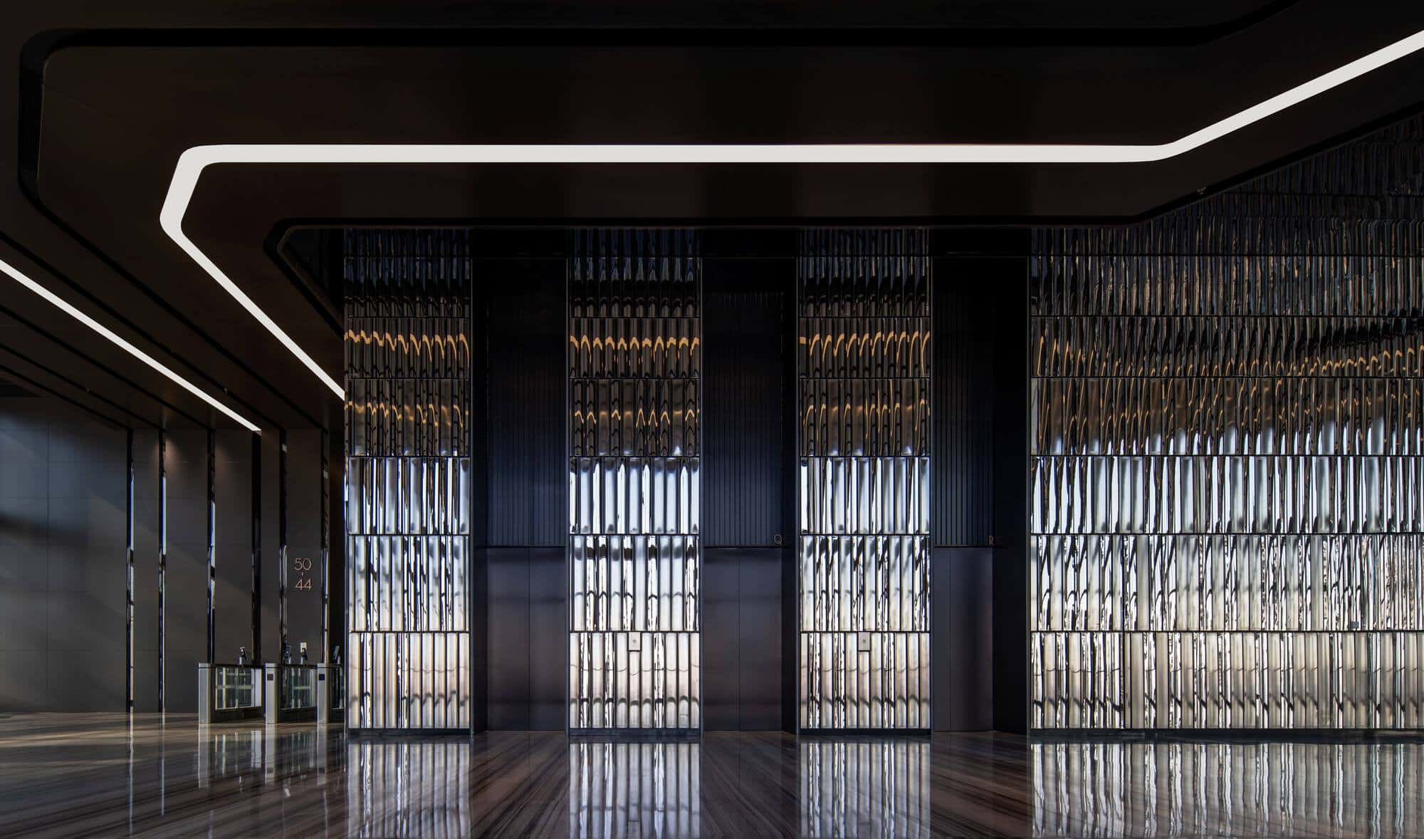 A wide-angle shot of a Jinan Tower interior hall featuring a textured metallic mirrored wall and a zigzag linear ceiling light.