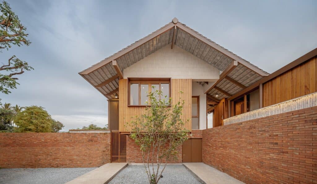 Modern Lanna house facade featuring a gabled roof, timber cladding, and a red brick boundary wall in Chiang Rai.