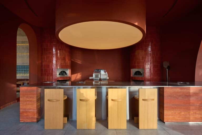 Modern open kitchen design in Blu Mare project featuring a circular terracotta structure, stainless steel counter, and wooden bar stools.