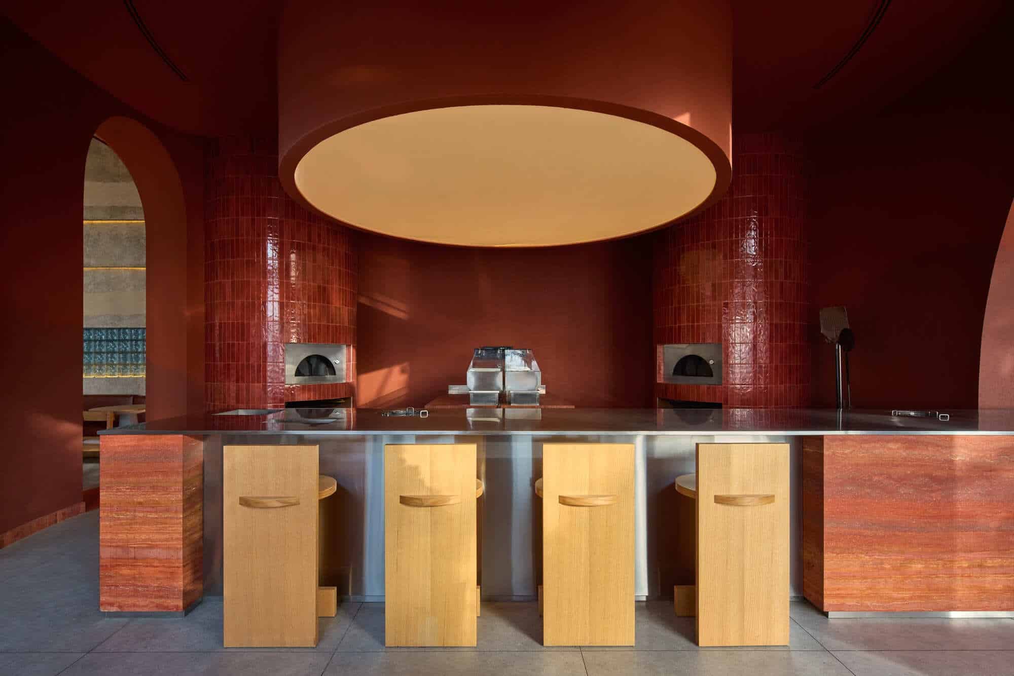 Modern open kitchen design in Blu Mare project featuring a circular terracotta structure, stainless steel counter, and wooden bar stools.