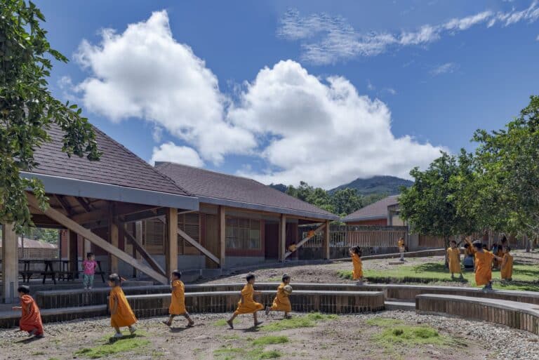 Children playing in the outdoor amphitheater and courtyard of Sonomoro School in Peru, featuring wooden structures and a central orange grove.