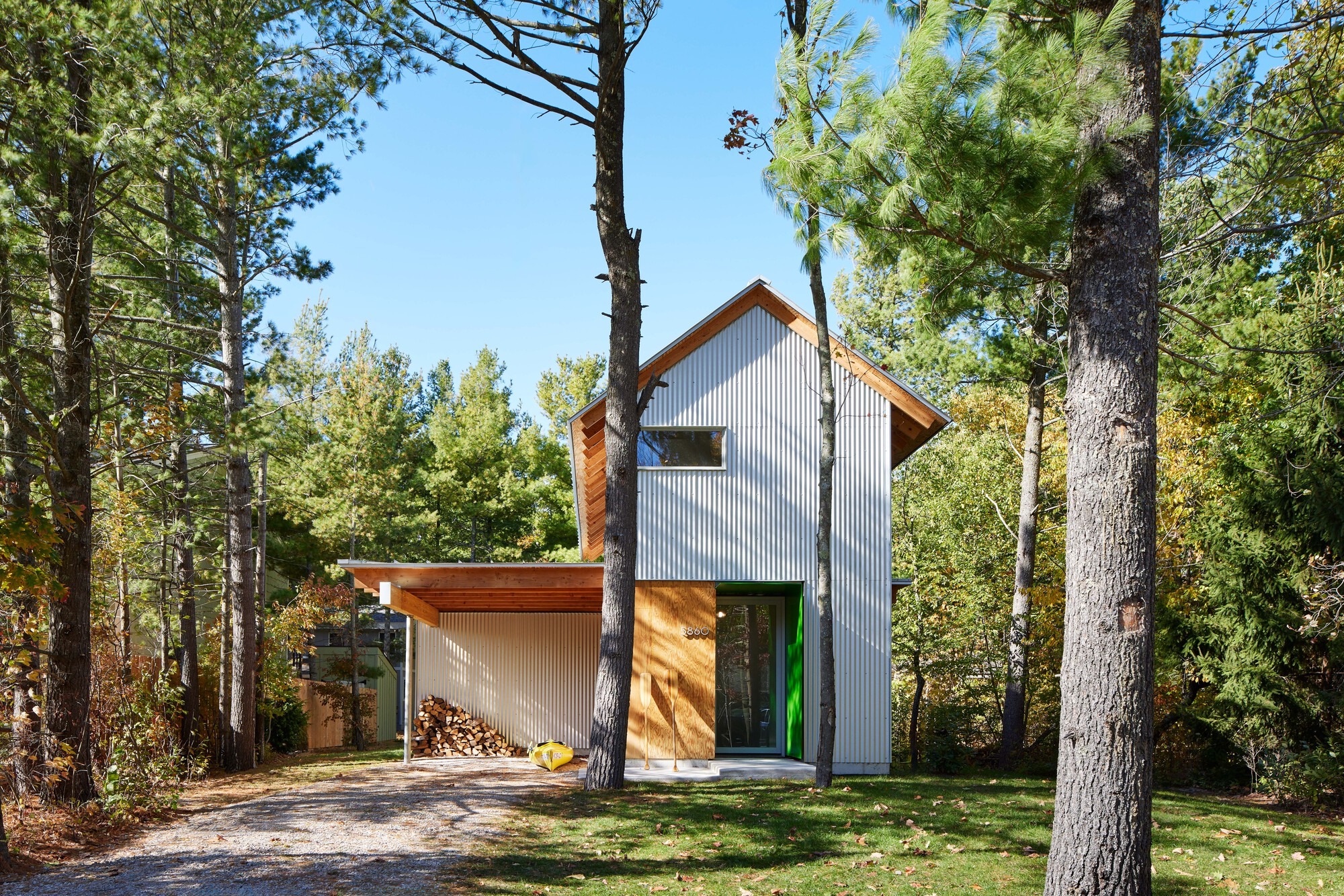 Exterior front view of Liten Hytte House showing corrugated metal cladding and wooden entrance nestled in a pine forest.