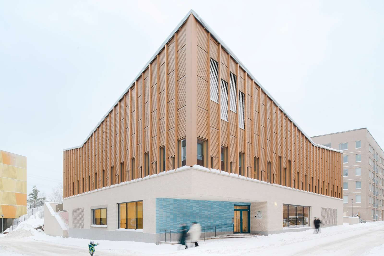 Exterior corner view of Postiljooni Daycare Centre showing the contrast between the stone ground floor and vertical wooden slats on the upper level in winter.