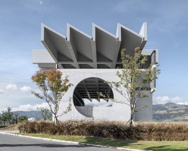 A brutalist concrete facade of the Xichang Documentary Museum featuring a large circular architectural opening and a rhythmic sawtooth roof.