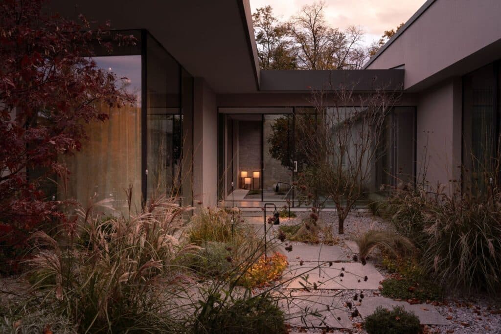 Exterior courtyard of a Lake Como villa featuring wild grasses, stone pathways, and large glass windows reflecting the sunset.