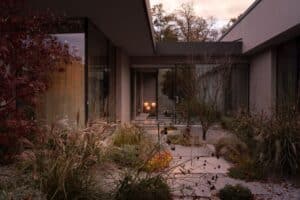 Exterior courtyard of a Lake Como villa featuring wild grasses, stone pathways, and large glass windows reflecting the sunset.