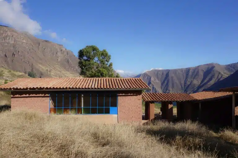 Exterior view of an adobe residential unit with a red tiled gable roof and large windows overlooking the Andes mountains.