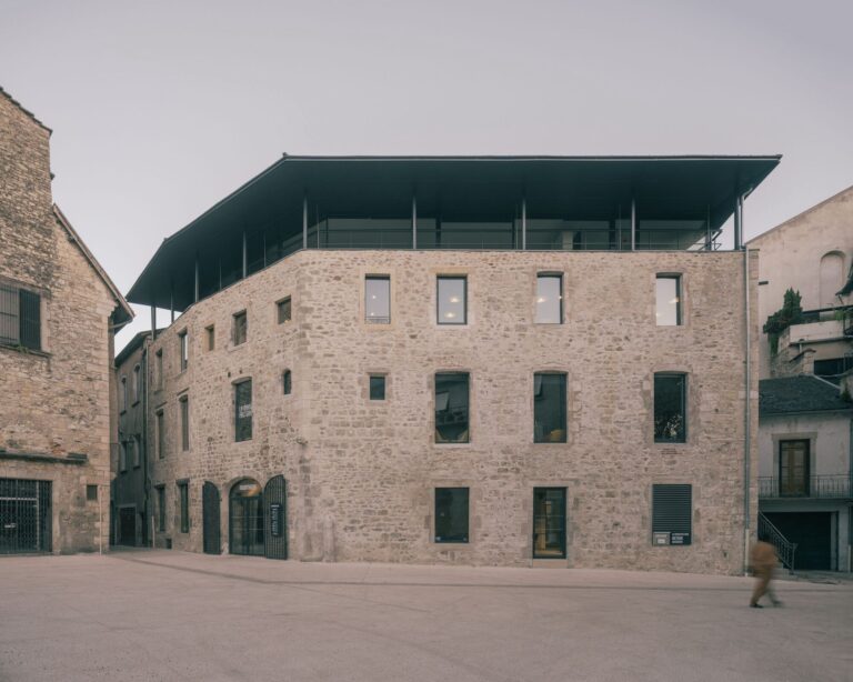 Exterior stone facade of La Manufacture Cultural Center showing the contrast between the historic masonry and the modern dark metal roof extension.