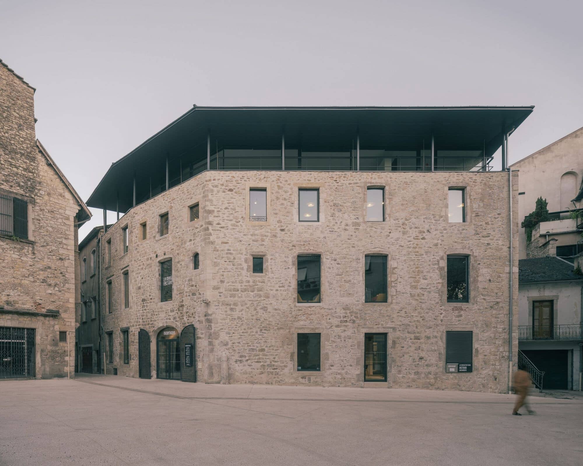 Exterior stone facade of La Manufacture Cultural Center showing the contrast between the historic masonry and the modern dark metal roof extension.