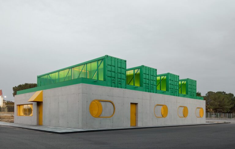 Exterior view of Agrosemillas offices featuring a concrete base with yellow circular windows and green shipping containers on the roof.