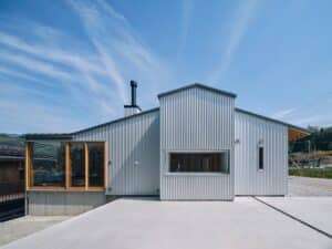 Exterior facade of the Kamioka office renovation showing corrugated metal cladding and large glass windows under a blue sky.