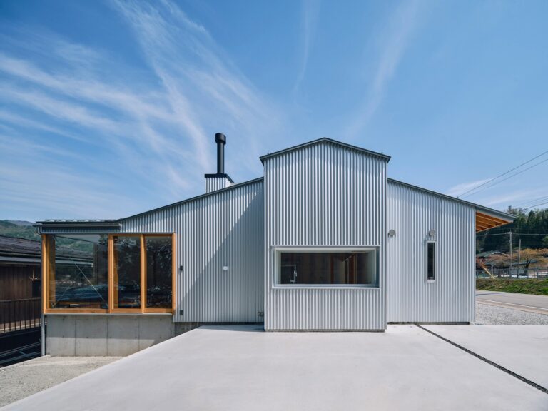 Exterior facade of the Kamioka office renovation showing corrugated metal cladding and large glass windows under a blue sky.