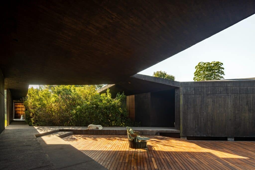 Interior courtyard of Casa Mavra with wooden decking, monolithic black concrete walls, and sharp architectural shadows.