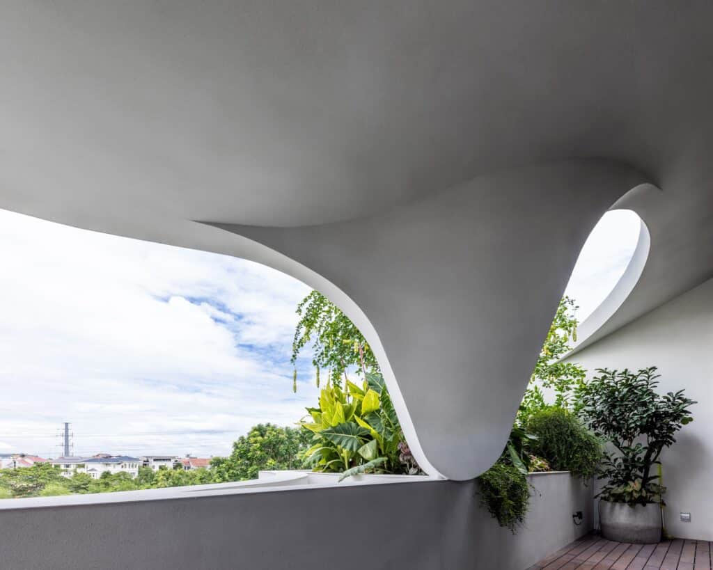 Close-up of a white sculptural concrete overhang with a curved opening looking out to a garden and blue sky.