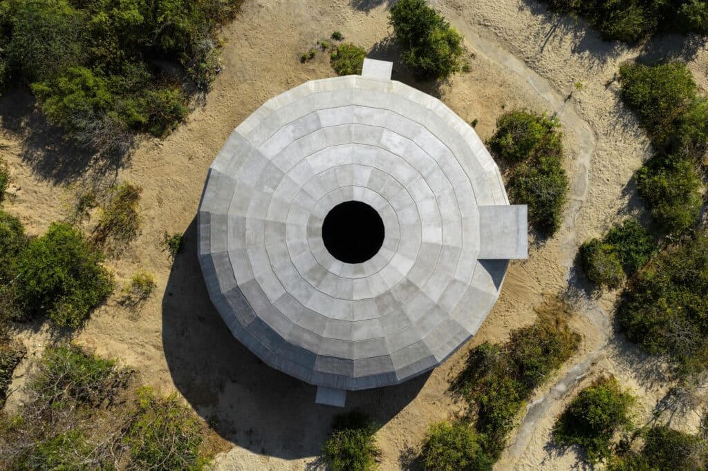 Aerial top-down view of the Mushroom Pavilion showing the central oculus and the circular concrete structure in the desert landscape.