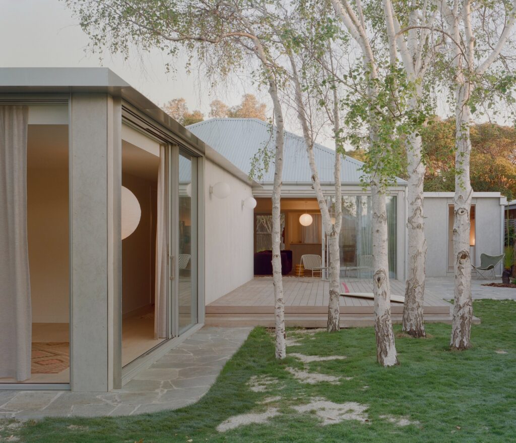 Rear view of Wood House featuring a timber deck, birch trees, and large sliding glass doors connecting the interior to the garden.