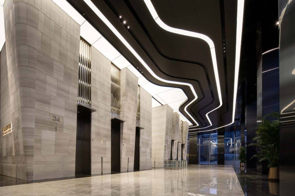 The grand lobby of Jinan Tower with towering beige sedimentary stone walls and a dark undulating ceiling with integrated linear lighting.