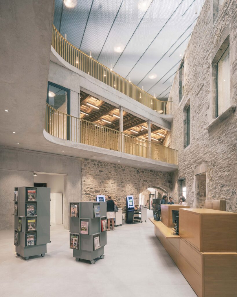 Interior view of the central atrium at La Manufacture Cultural Center with a wooden reception desk and stone walls under a skylight.