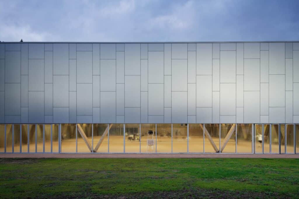Close-up of the metallic panel facade of the Sporting Vichy tennis hall with a horizontal glass strip revealing the interior clay courts.