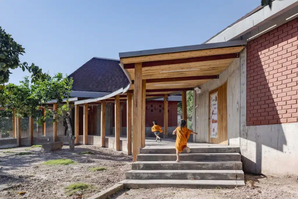 A semi-circular wooden corridor with a bamboo ceiling at Sonomoro School, leading children toward the classroom blocks.