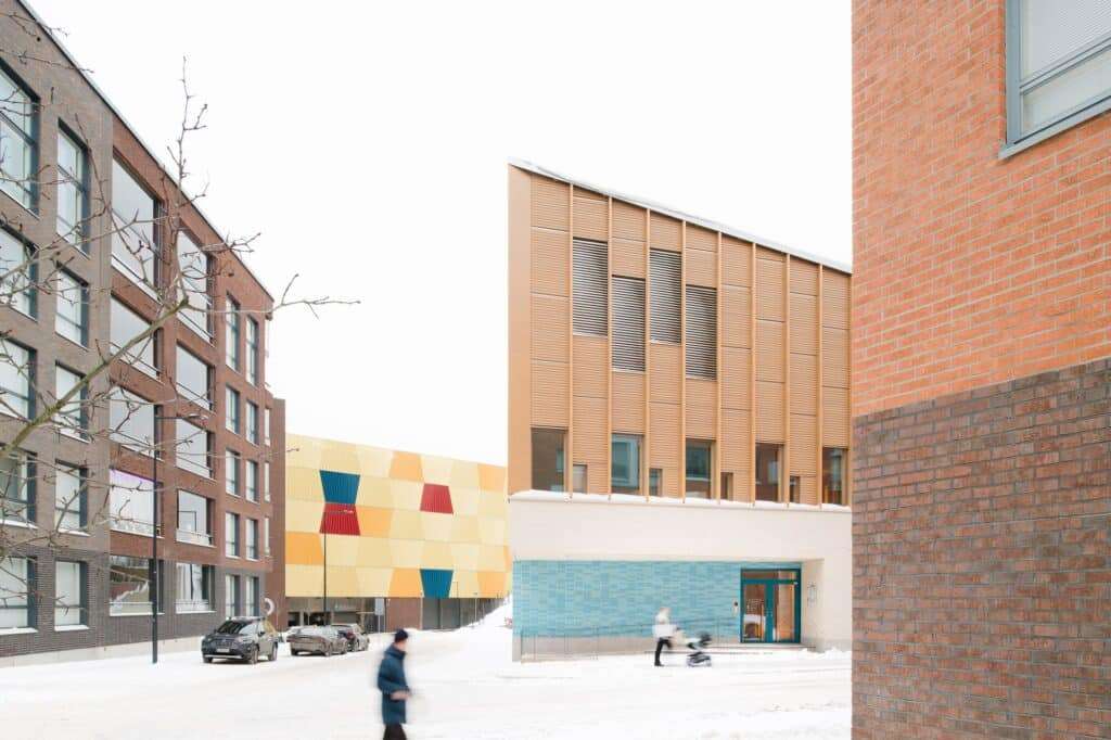 Postiljooni Daycare Centre integrated into a modern residential neighborhood with snow-covered streets and surrounding brick buildings.