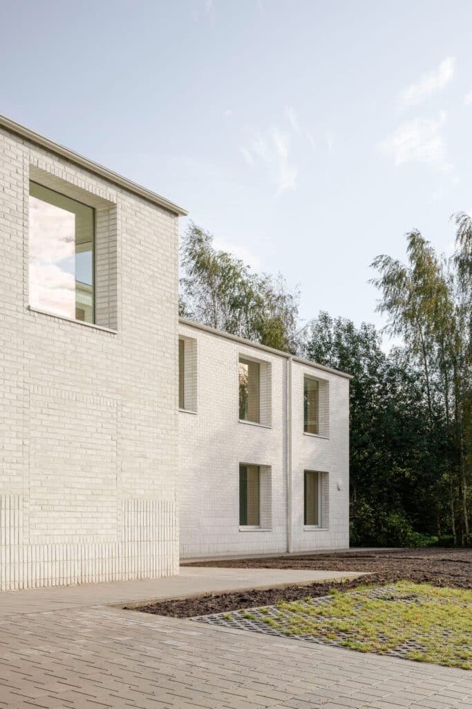 Low-angle architectural shot of Care Villa's white brick walls and large windows, showcasing the texture and the integration with surrounding greenery.