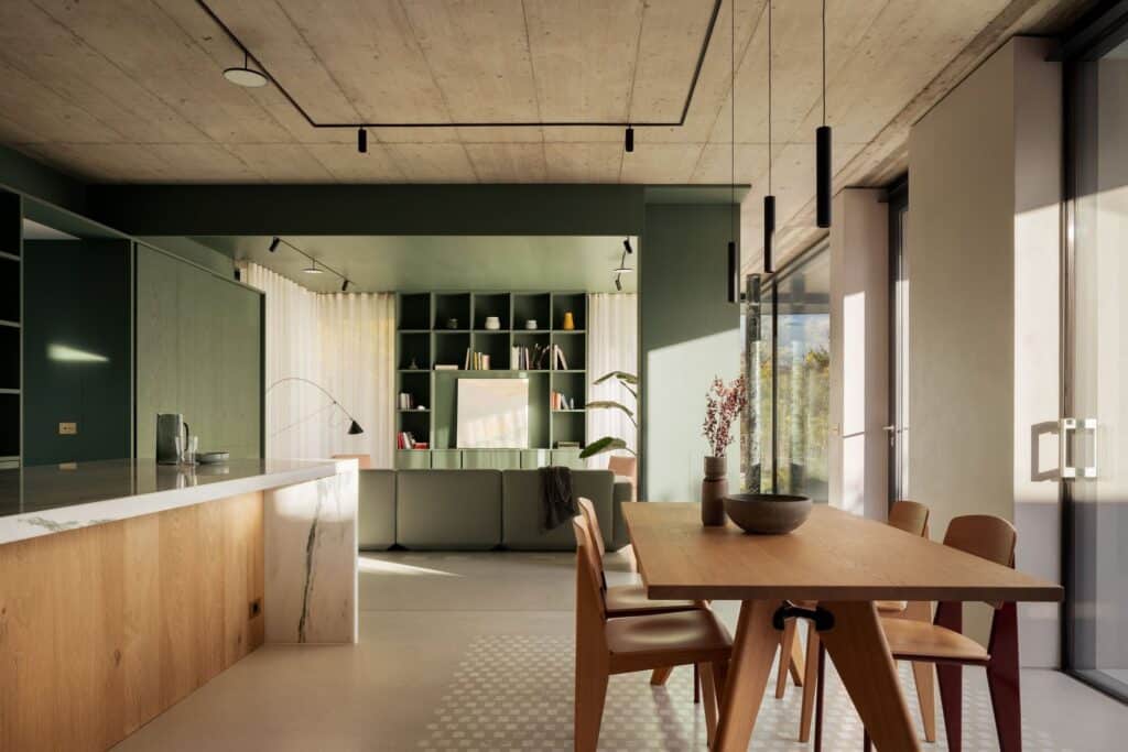 Open-plan interior of a modern villa with green cabinetry, raw concrete ceiling, and a wooden dining table overlooking Lake Como.