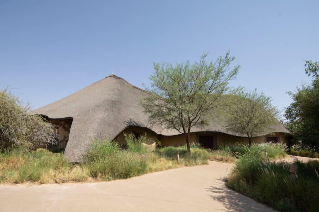 Main entrance building of Sharjah Bridi Park featuring a large undulating thatched roof.