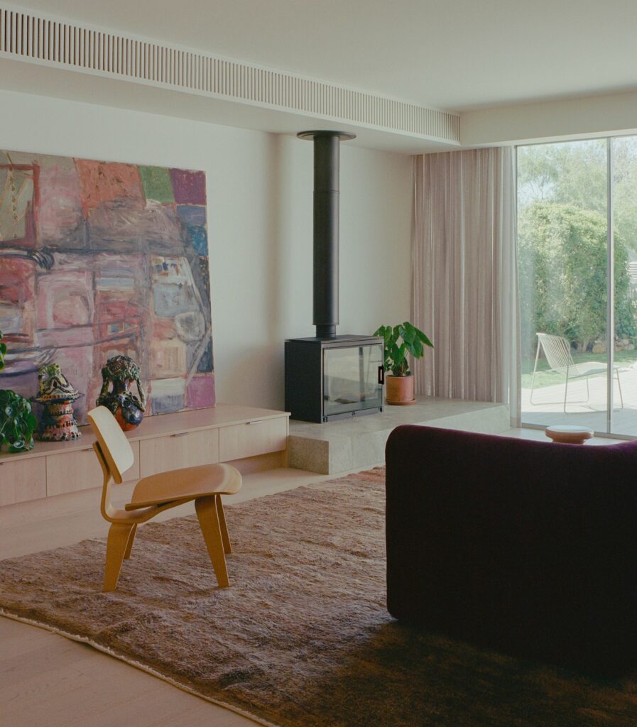 Modern living room interior with a black fireplace, large abstract painting, timber flooring, and a view of the garden through glass doors.