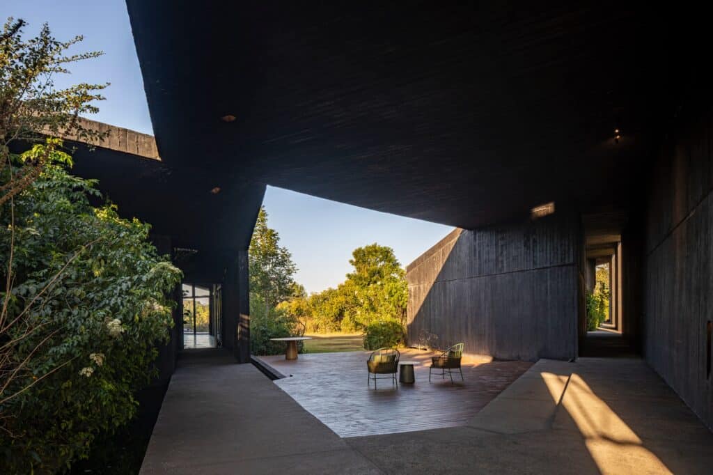 A minimalist hallway and outdoor terrace at Casa Mavra with textured black concrete walls and a view of the forest.