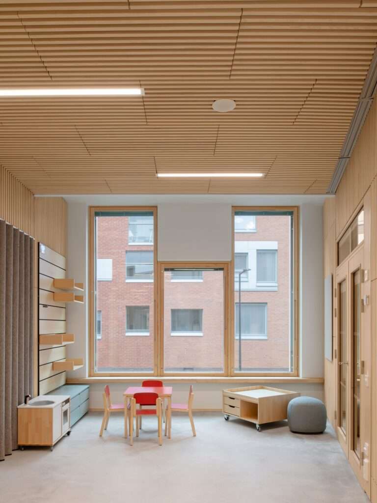 Interior classroom of Postiljooni Daycare featuring ash wood ceilings, large windows, and colorful children's furniture.