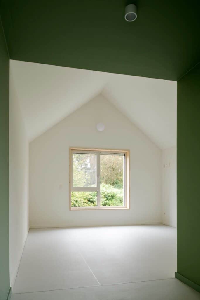 Interior of a residential unit in Care Villa featuring a high pitched ceiling, white walls, green accents, and a large window overlooking trees.