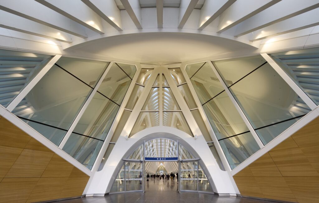 Symmetrical view of a glass entrance portal inside Mons Train Station with white structural beams and wooden wall panels.
