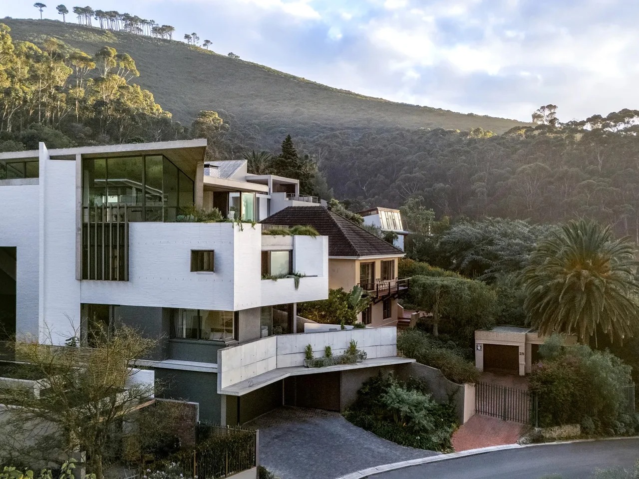 Exterior view of Kenmore House, a multi-level modern residence built on a steep slope with white textured walls and expansive glass windows.