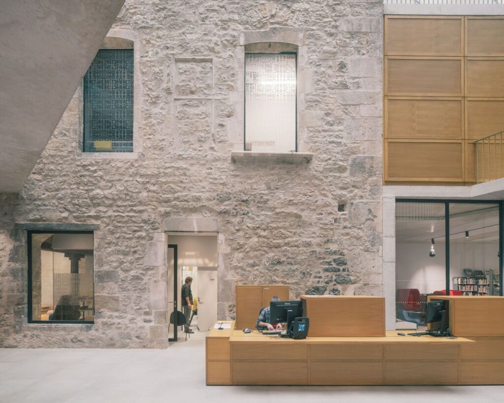 Close-up of the historic stone wall interior at La Manufacture with modern wooden furniture and glass partitions.