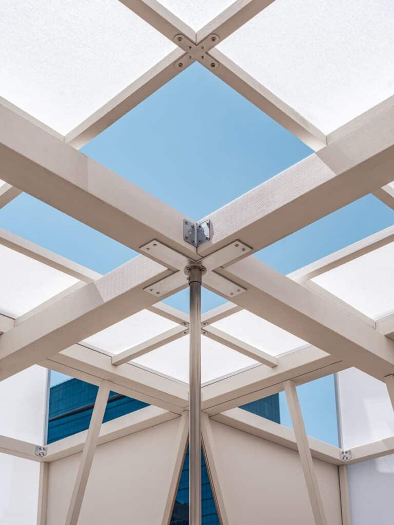 Low angle shot looking up at the sky through the gridded white structure and central pole of the pavilion.