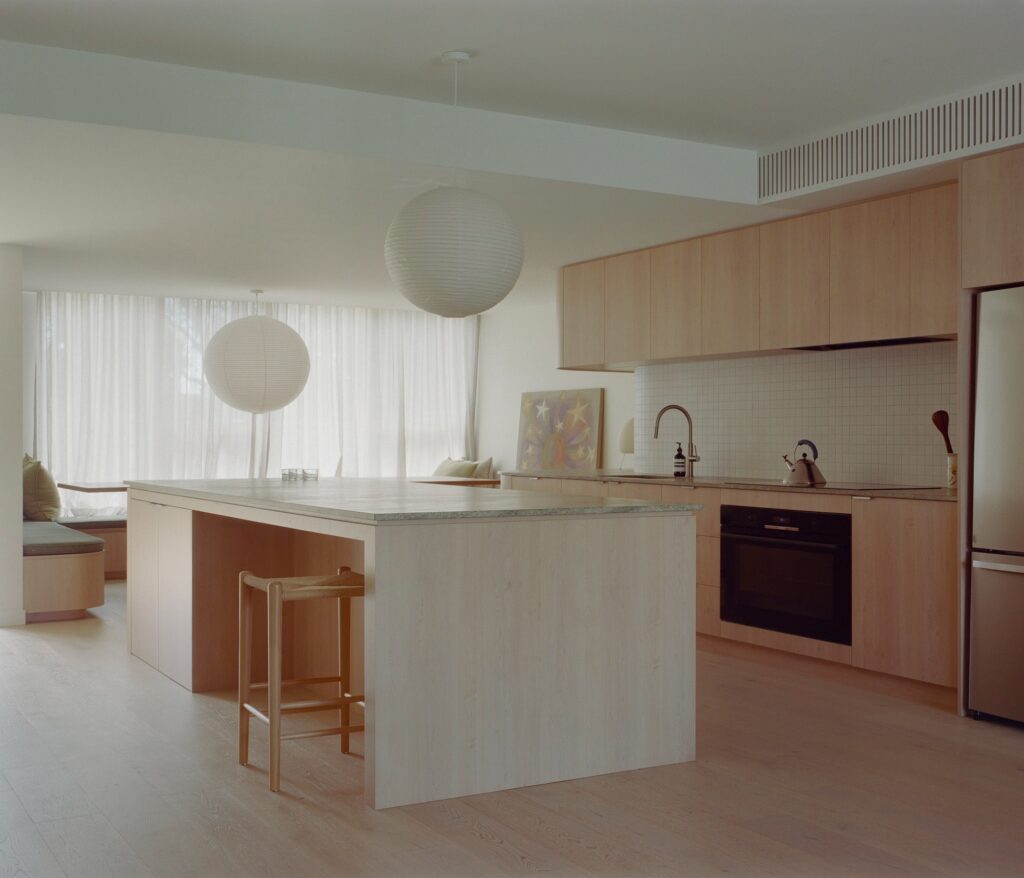 Minimalist kitchen with light wood cabinetry, a large kitchen island, and spherical paper pendant lights.