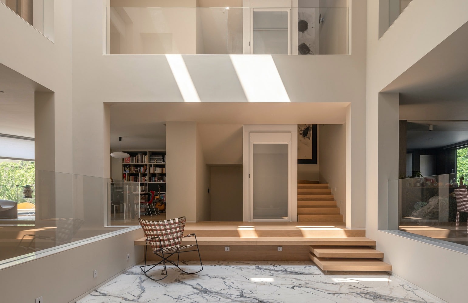 Interior view of the central light well in the House of Porous, showing a marble-floored courtyard, wooden steps, and glass railings with natural sunlight streaming from above in a multi-generational home.