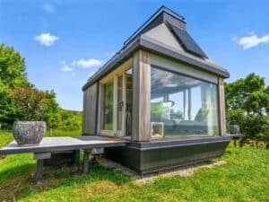 Exterior view of the Devin Cabin, a modern micro-dwelling with large glass windows and solar panels on a green hillside.