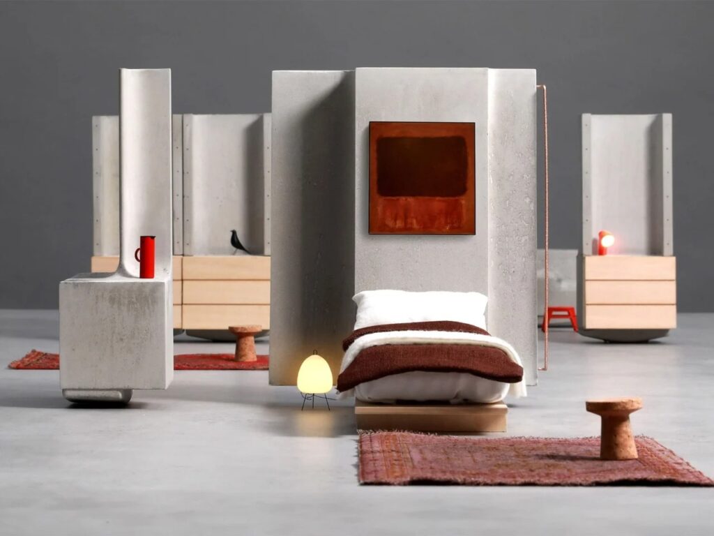 MIT Heirloom House interior setup featuring modular concrete walls, a bed, and minimalist furniture on a rug.