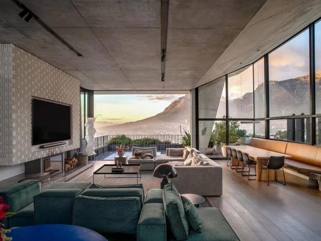 Open-plan living and dining area in Kenmore House featuring floor-to-ceiling windows with a panoramic view of a mountain landscape at sunset.