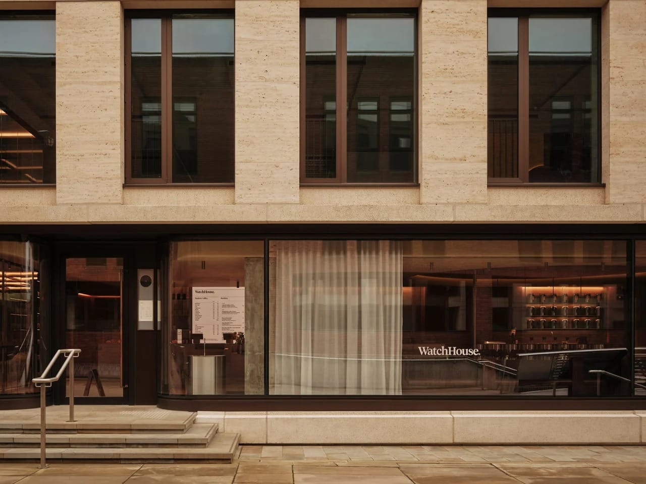 Exterior facade of WatchHouse cafe on the River Thames featuring large glass windows and stone architecture.