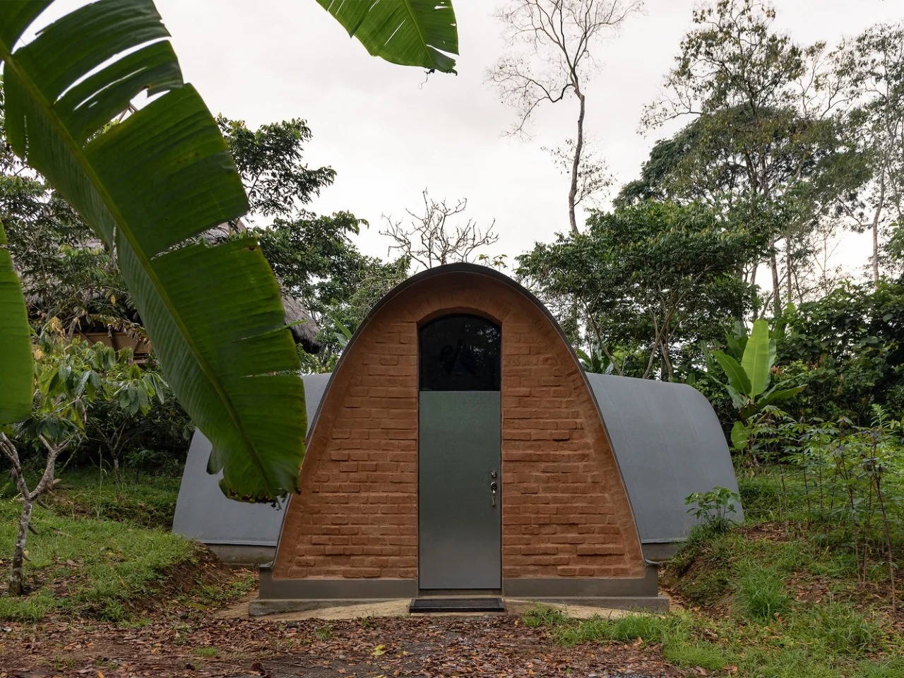 Front view of Witocha Lab in Ecuador, featuring a vaulted adobe brick entrance and a sealed metal door surrounded by Amazonian vegetation.